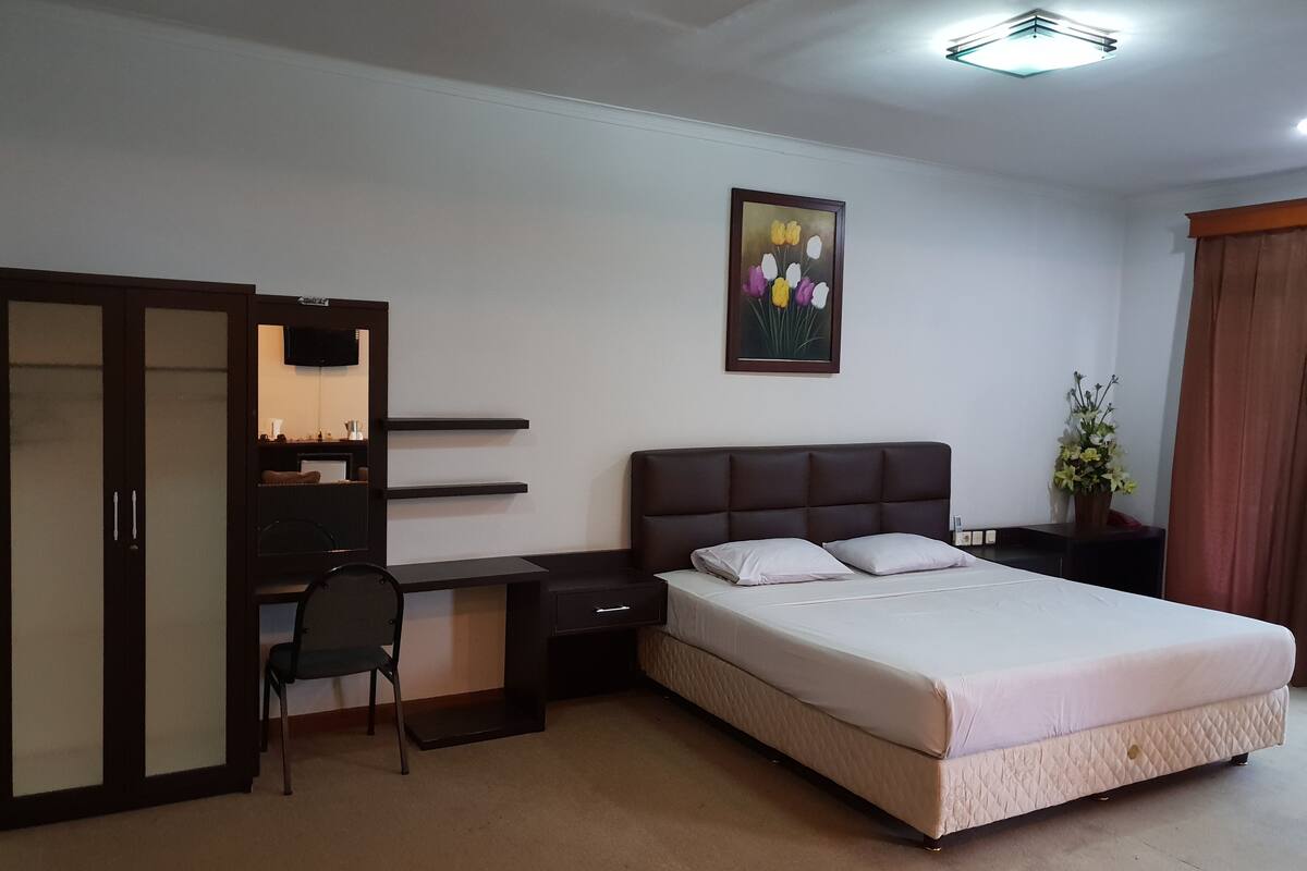 A bedroom with a bed, a desk, a chair, a wardrobe, and a painting on the wall.