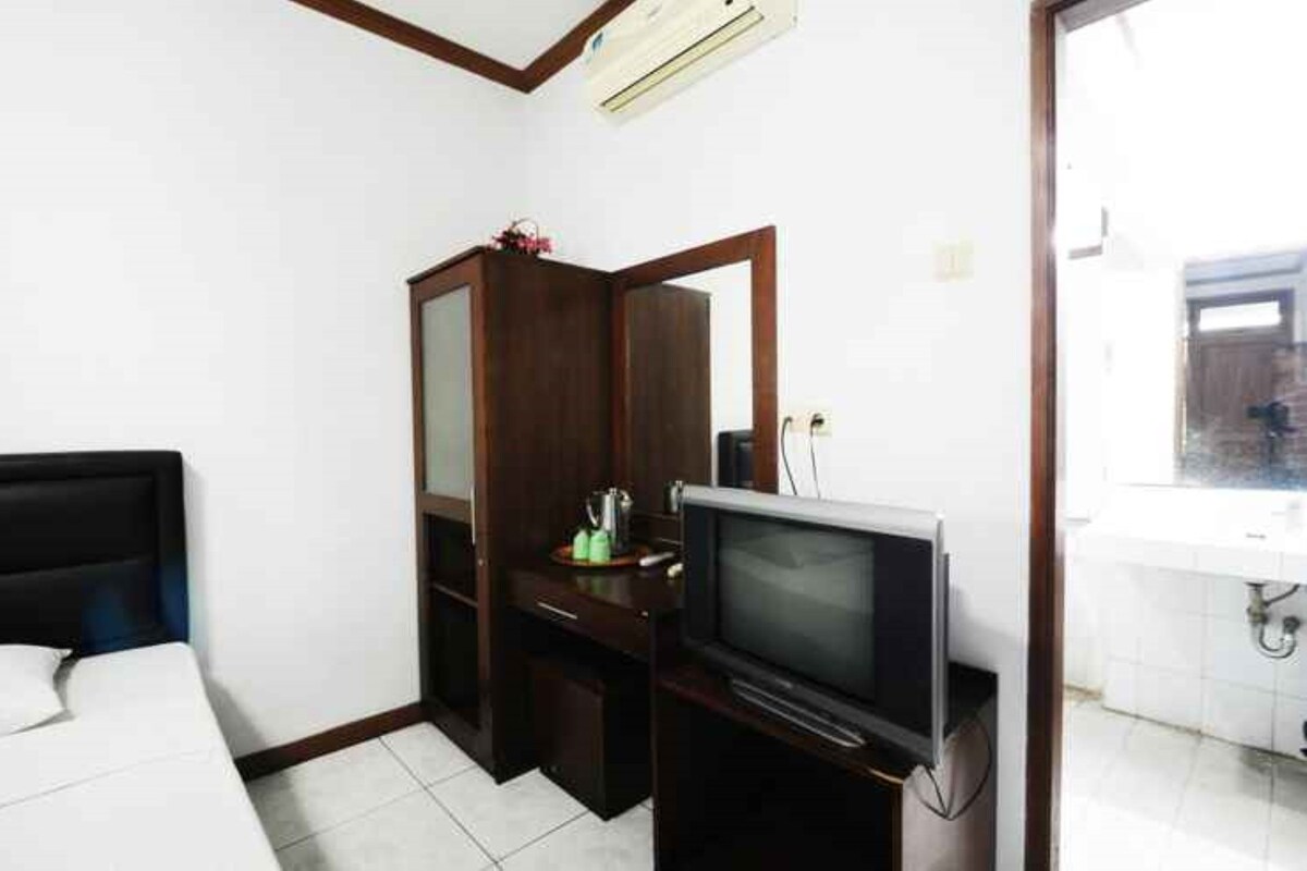 Een kleine hotelkamer met een bed, een televisie, een houten garderobe en een zichtbare badkamer door een geopende deur.