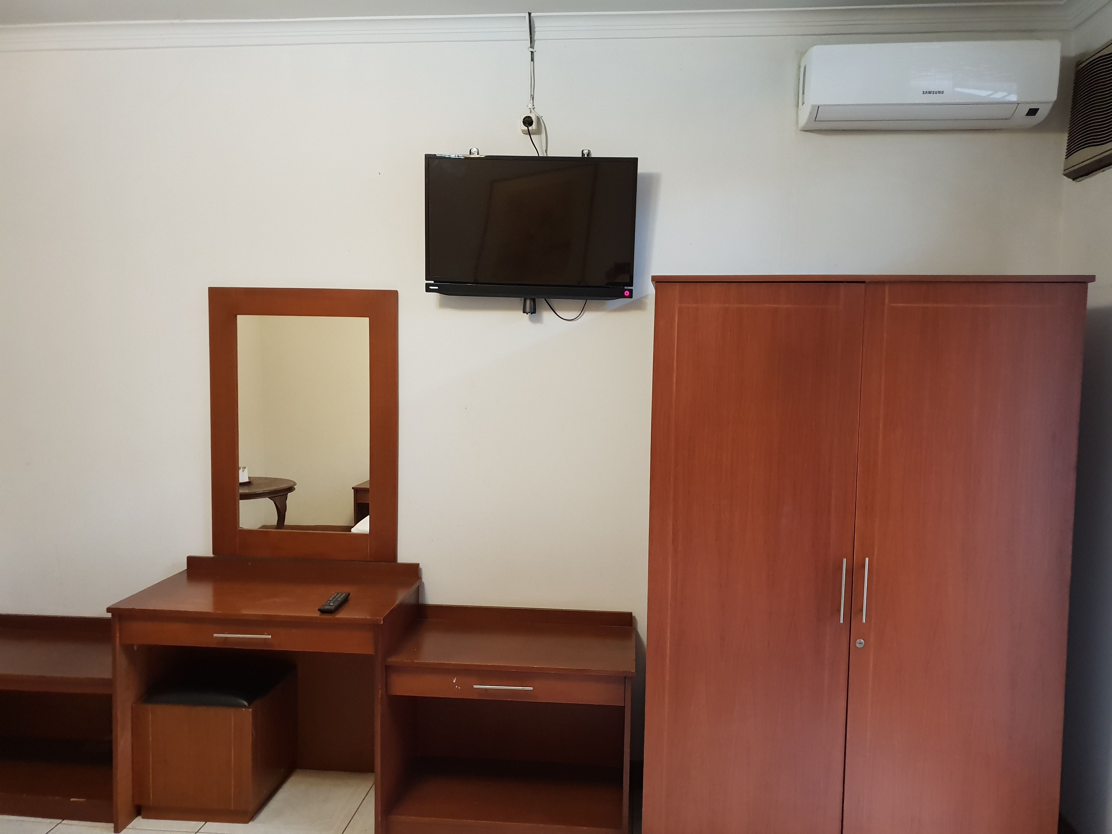 Une pièce comprenant un bureau en bois, un miroir, un téléviseur fixé au mur et une armoire.
