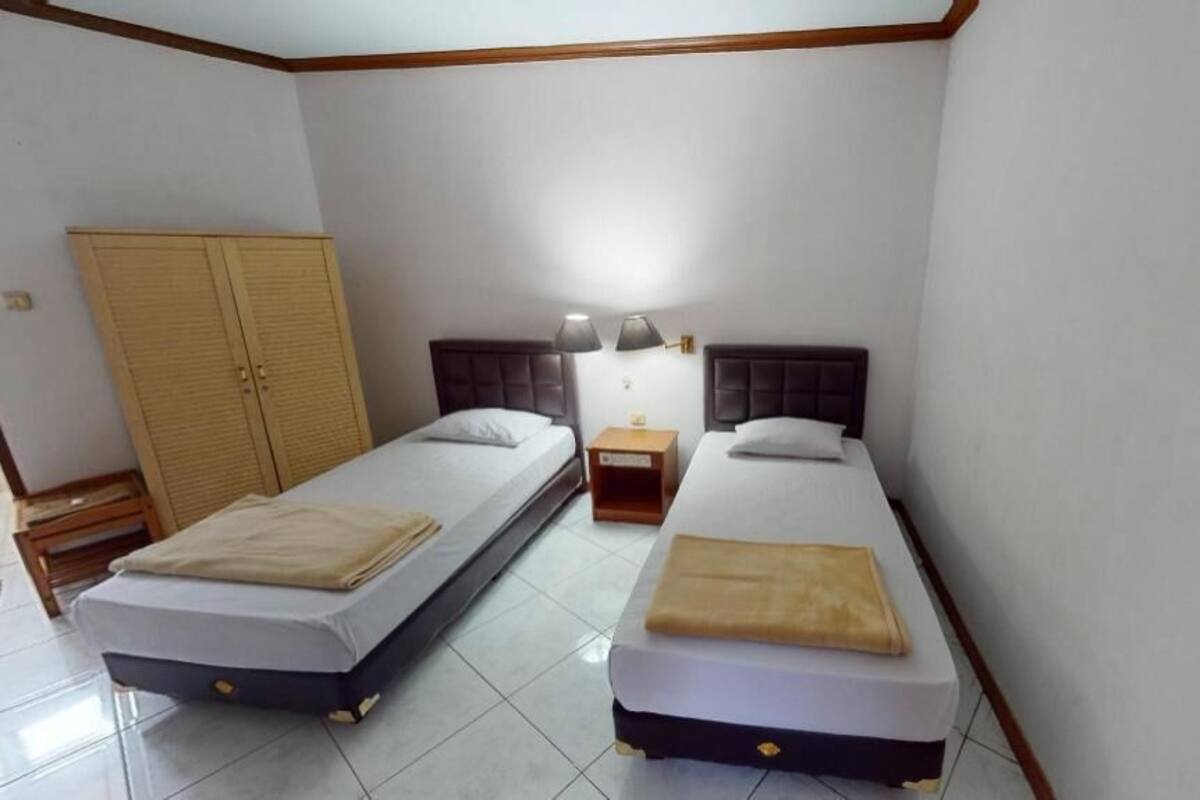 A room with two beds, a wardrobe, a nightstand, and a lamp.