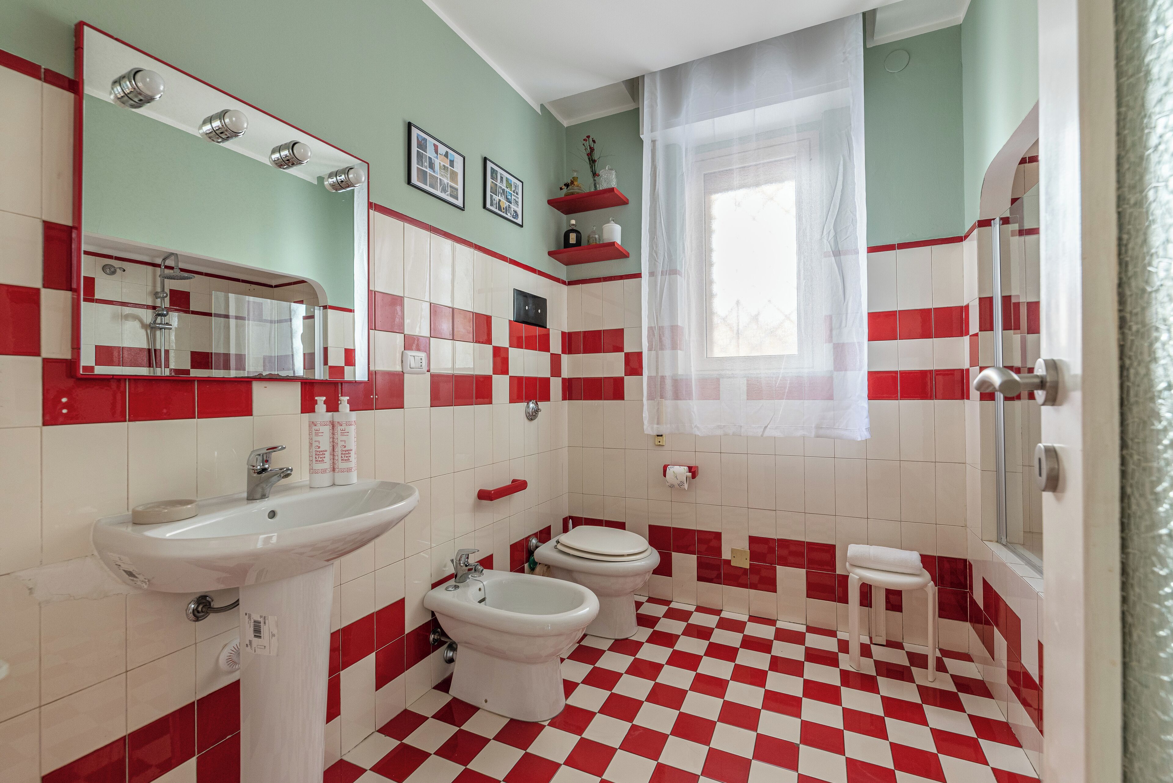 A bathroom with a checkered floor, a sink, a bidet, a toilet, a shower, and a mirror with lights.
