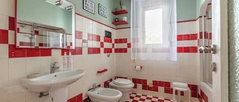 A bathroom with a checkered floor, a sink, a bidet, a toilet, a shower, and a mirror with lights.