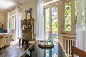 A room with a wooden floor, a round table, a mirror, a sofa, and a view of greenery outside.
