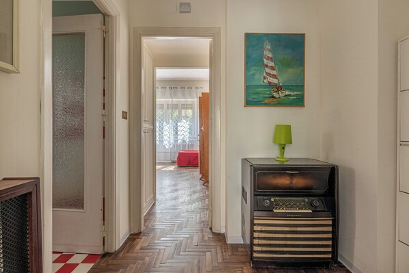 A hallway with a herringbone floor, a vintage radio, and a painting of a sailboat on the wall.