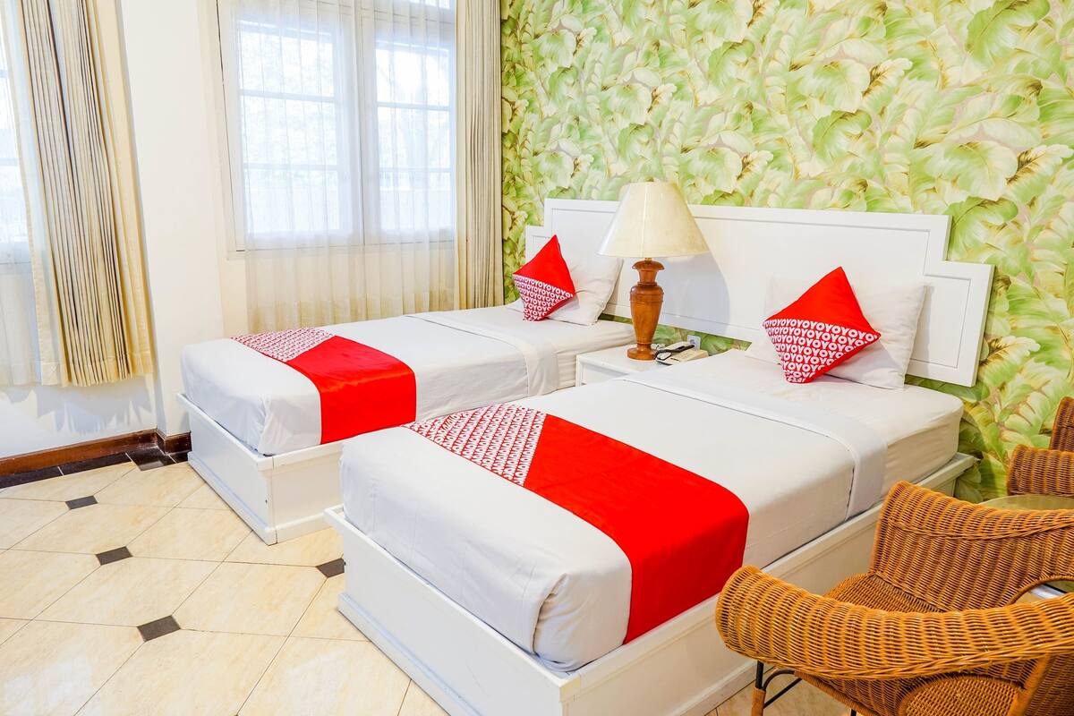 Une chambre d’hôtel avec deux lits, chacun recouvert d’une courtepointe rouge et blanche, doté d’une tête de lit blanche et muni d’une table de chevet avec une lampe.