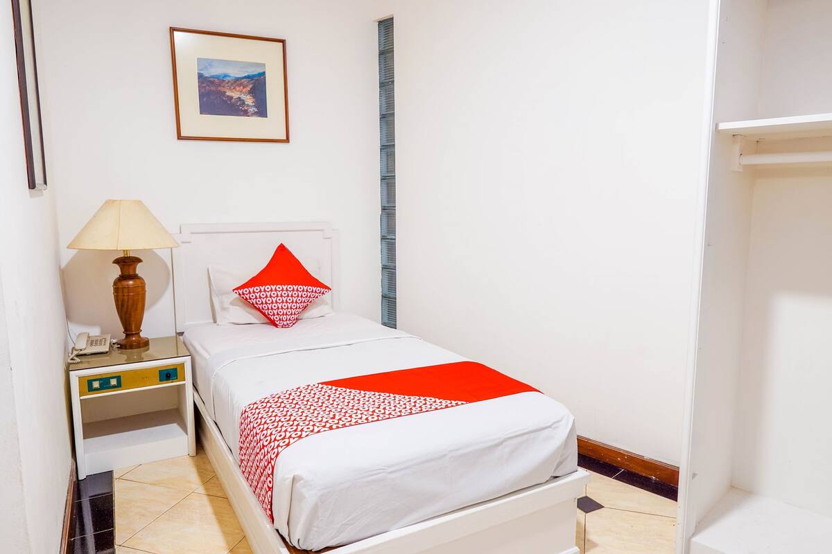 Une chambre d’hôtel avec un lit, une table de chevet avec une lampe, un téléphone et un tableau encadré au mur.