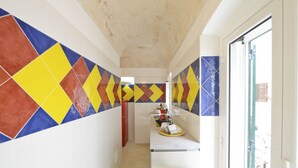 A narrow hallway with colorful geometric tiles on the walls, a white countertop with a sink, and a door leading to a balcony. - Isabella Apartments by Wonderful Italy (Ostuni)