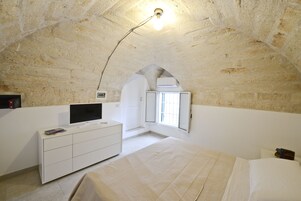 Quarto com teto de pedra, uma cama, uma televisão sobre uma cômoda branca e uma janela com vista.