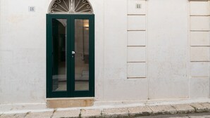 A green door with a decorative arch above it, set in a white building with numbered windows. - Isabella Apartments by Wonderful Italy (Ostuni)
