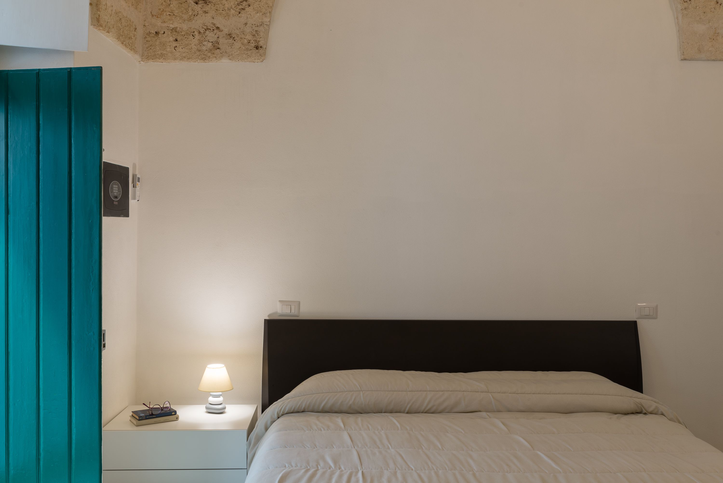 Un dormitorio con una cama, una mesita de noche, una lámpara y una puerta color turquesa.