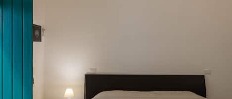 Un dormitorio con una cama, una mesita de noche, una lámpara y una puerta color turquesa.