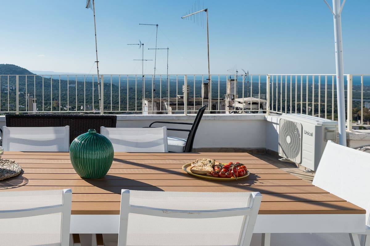 A rooftop terrace with a wooden table, white chairs, and a view of the cityscape.