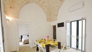 A room with a bed, a dining table with chairs, a small kitchen area, and a balcony with a metal railing. - Isabella Apartments by Wonderful Italy (Ostuni)