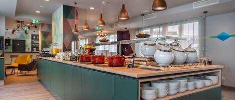 Una cocina moderna con una isla central, equipada con diversos electrodomésticos y utensilios, y una zona de estar con sillas.