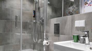 A modern bathroom with a glass-enclosed shower, a white sink, and a green and gray soap dispenser.
