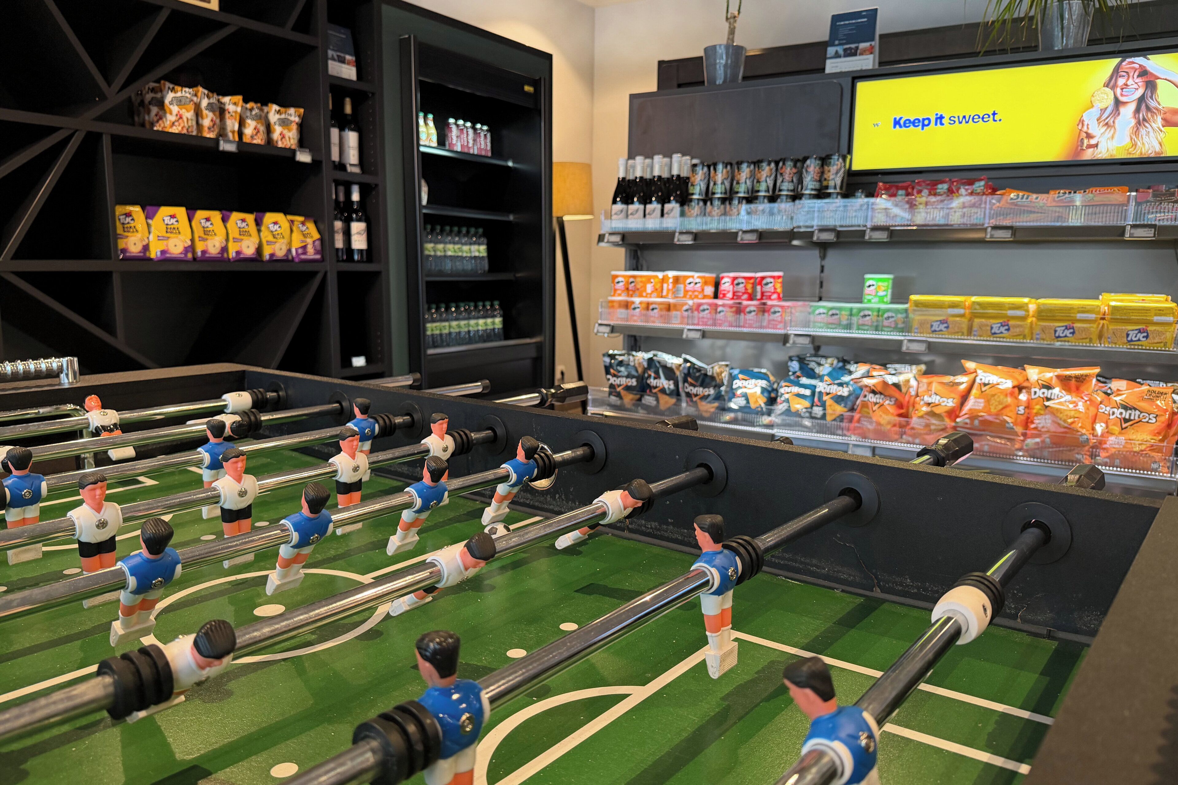 A foosball table, shelves with snacks, and a TV screen with a message.