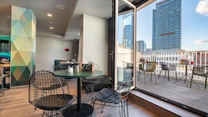 Un comedor moderno con una mesa redonda y sillas de estructura metálica, una pared de acento verde y vistas de un paisaje urbano a través de ventanas amplias.