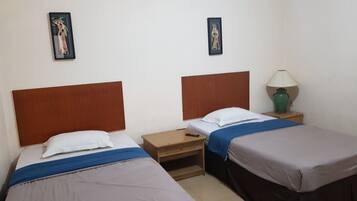 A hotel room with two beds, a nightstand, a lamp, and two framed pictures on the wall.
