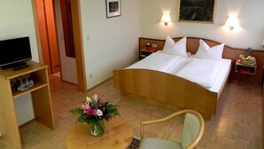 Une chambre d’hôtel avec un lit, un téléviseur posé sur un meuble, une chaise, une petite table avec un vase de fleurs et un tableau accroché au mur.