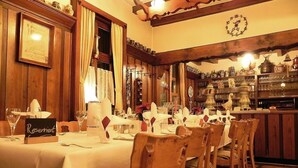 Un restaurant avec une longue table dressée pour un repas, des chaises en bois et un bar avec des étagères remplies de bouteilles et de verres.
