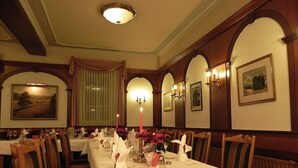 Une salle à manger élégante, avec de longues tables, des chaises en bois et des lustres.