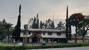 A two-story building with a central entrance, surrounded by greenery and tall trees. - Hotel Cisarua Indah (Cisarua)