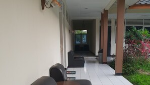 A covered outdoor seating area with black leather chairs and small round tables, a tiled floor, and a view of a building entrance in the background. - Hotel Cisarua Indah (Cisarua)