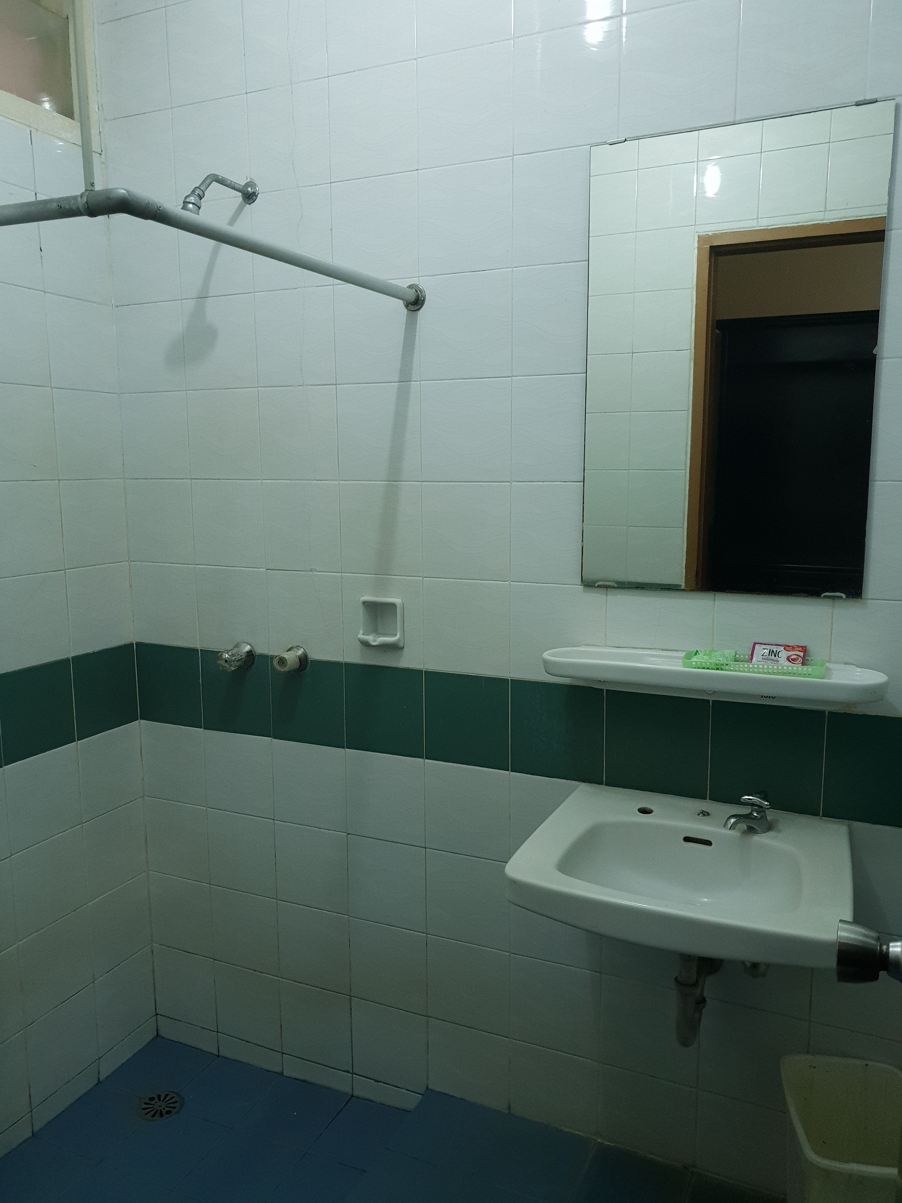 A bathroom with white and green tiles, a sink, a mirror, and a shower area.