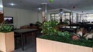 A spacious indoor area with multiple seating arrangements, including tables and chairs. There are several potted plants placed around the room, and a television is mounted on the wall. - Hotel Cisarua Indah (Cisarua)