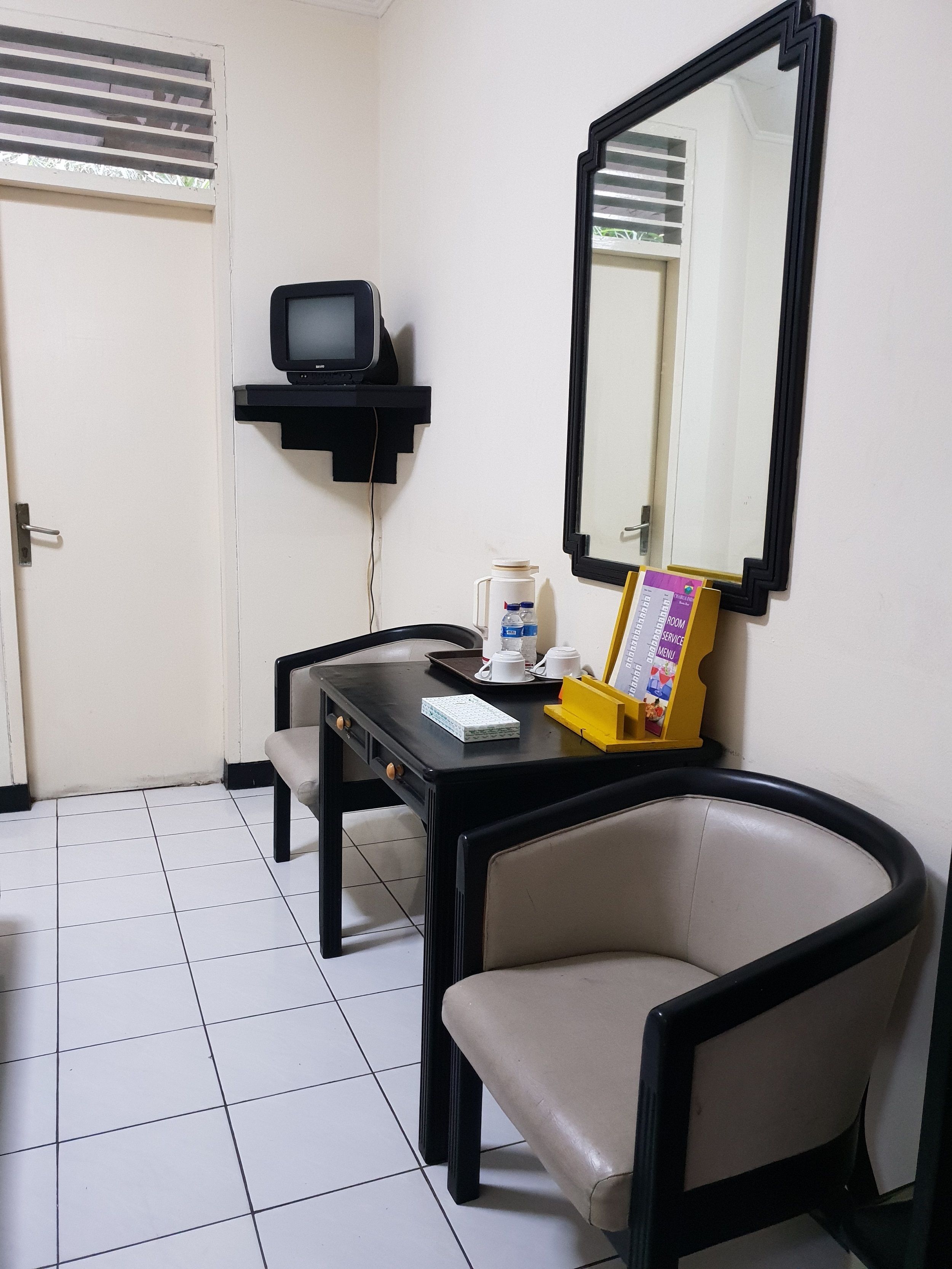 A small room with a desk, chair, a television, a mirror, and a door.