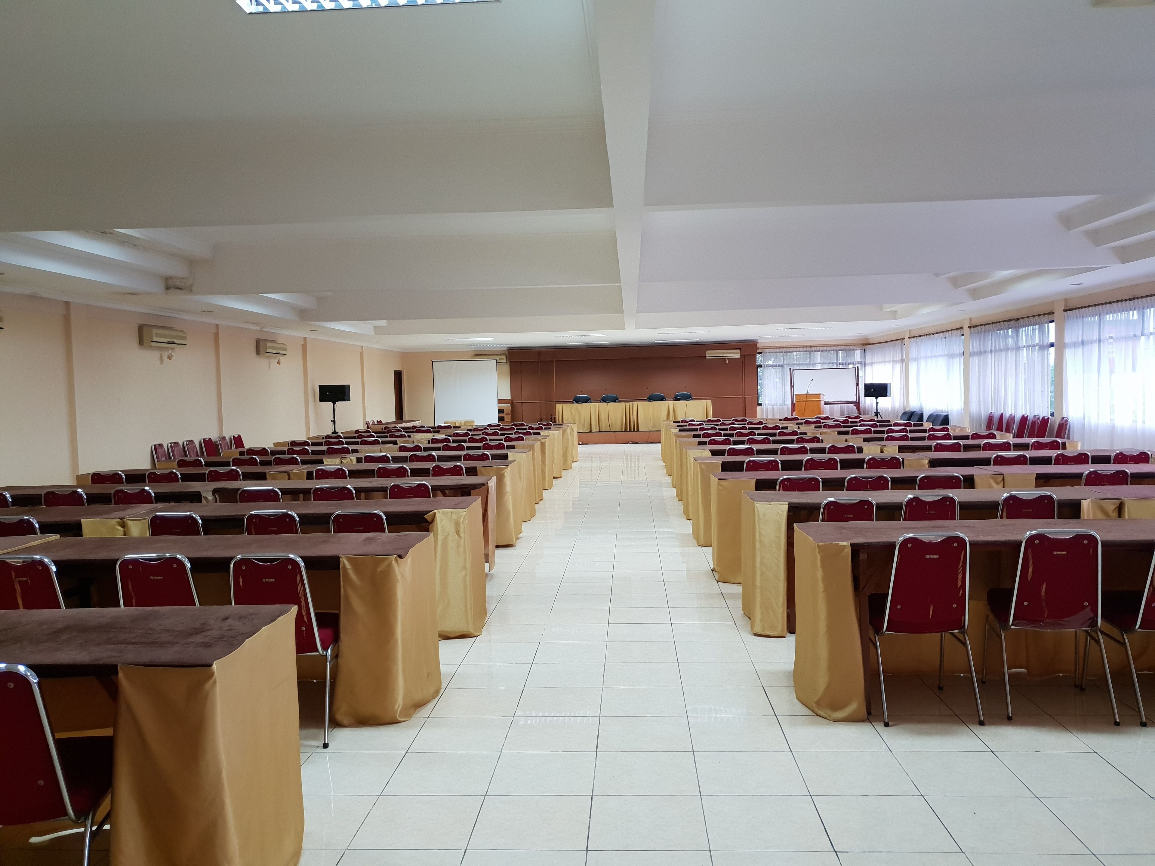 A large conference room with rows of tables and chairs, a podium, and a screen at the front.