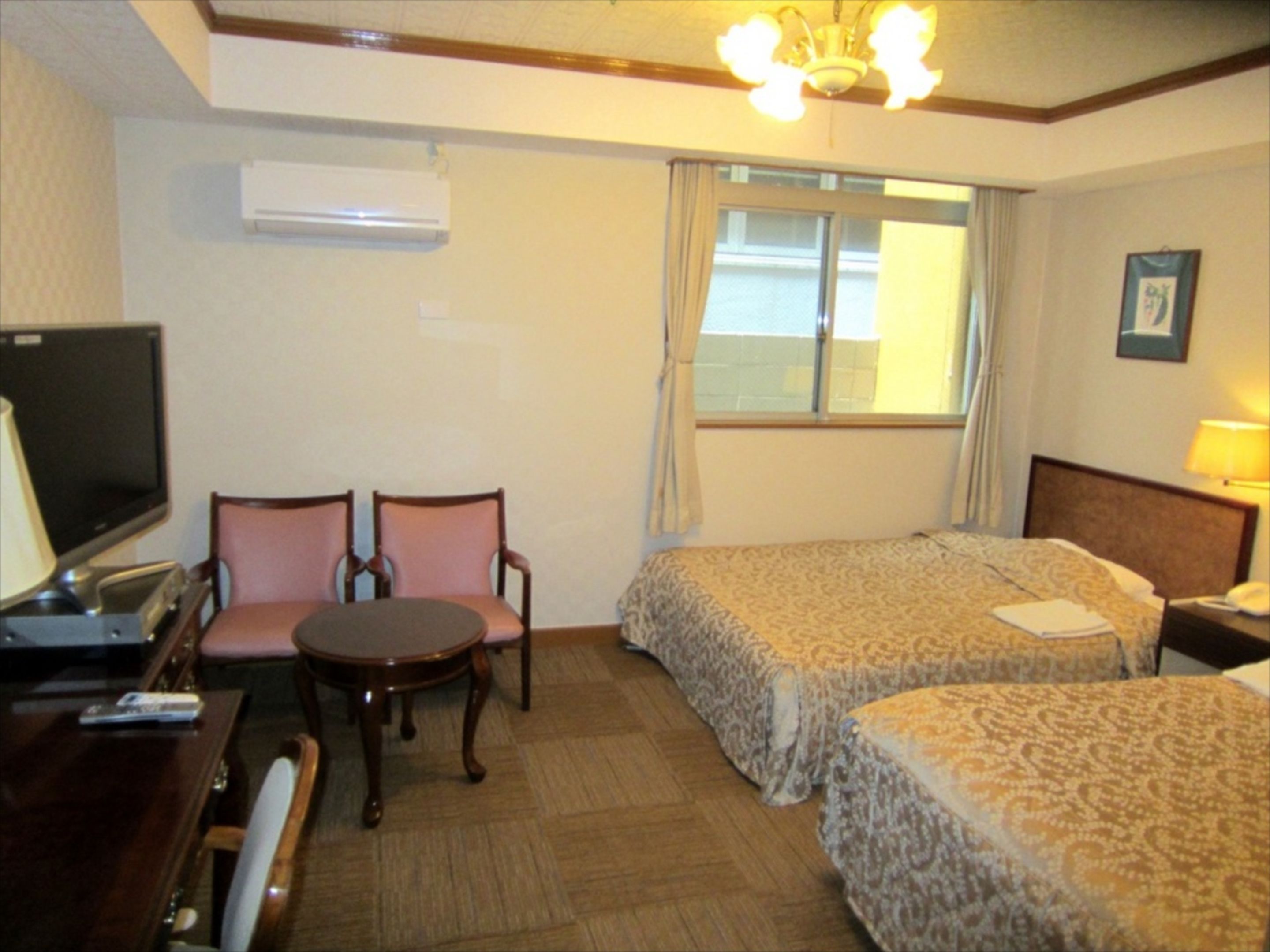 A hotel room with two beds, a desk with a TV, a small table, and chairs.