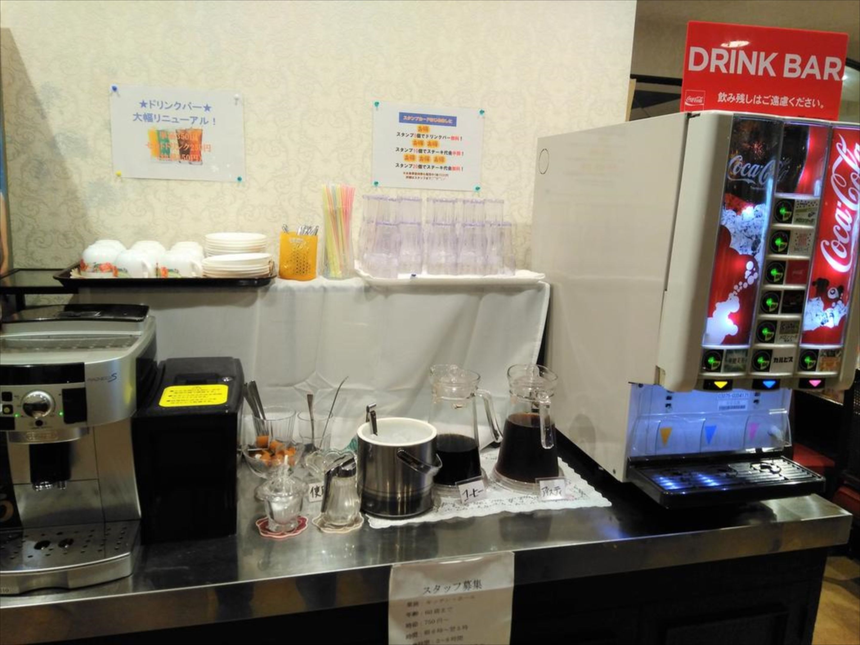 Una barra de desayuno con una máquina expendedora de Coca-Cola, una cafetera y diferentes opciones para el desayuno.