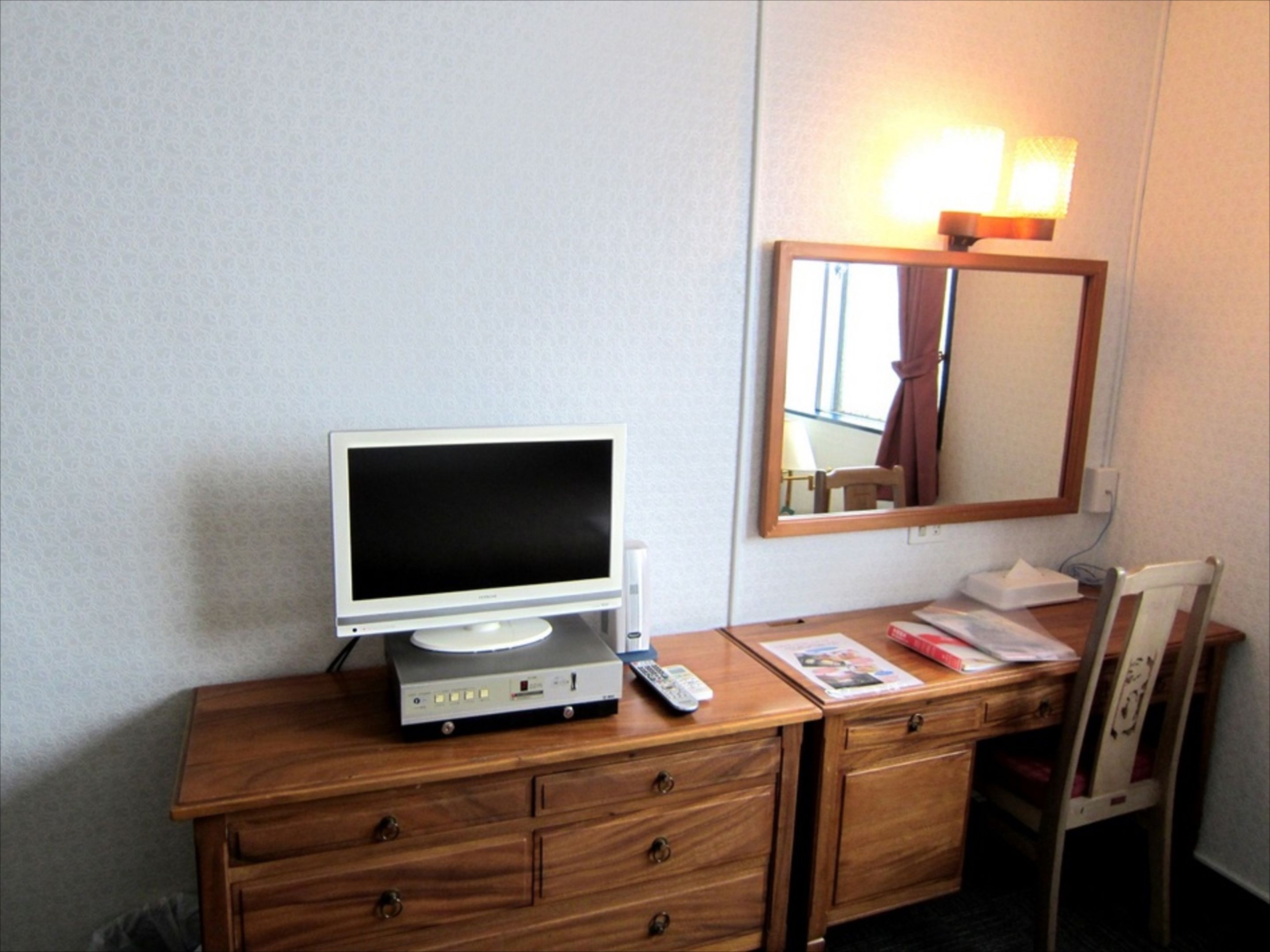 Un escritorio de madera con un televisor, un espejo y una silla.