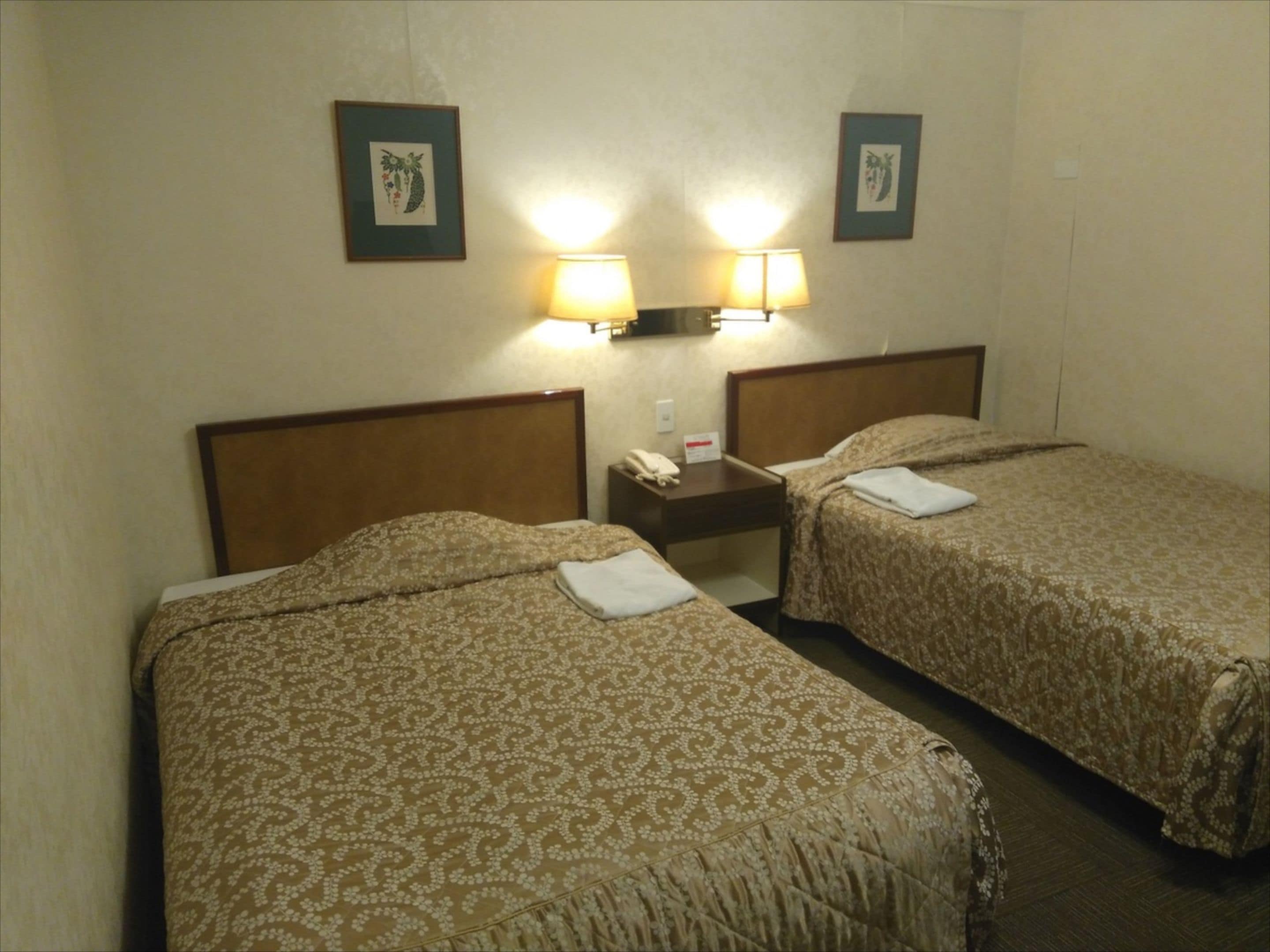 A hotel room with two beds, each with a patterned bedspread, a nightstand with a lamp, and framed pictures on the wall.