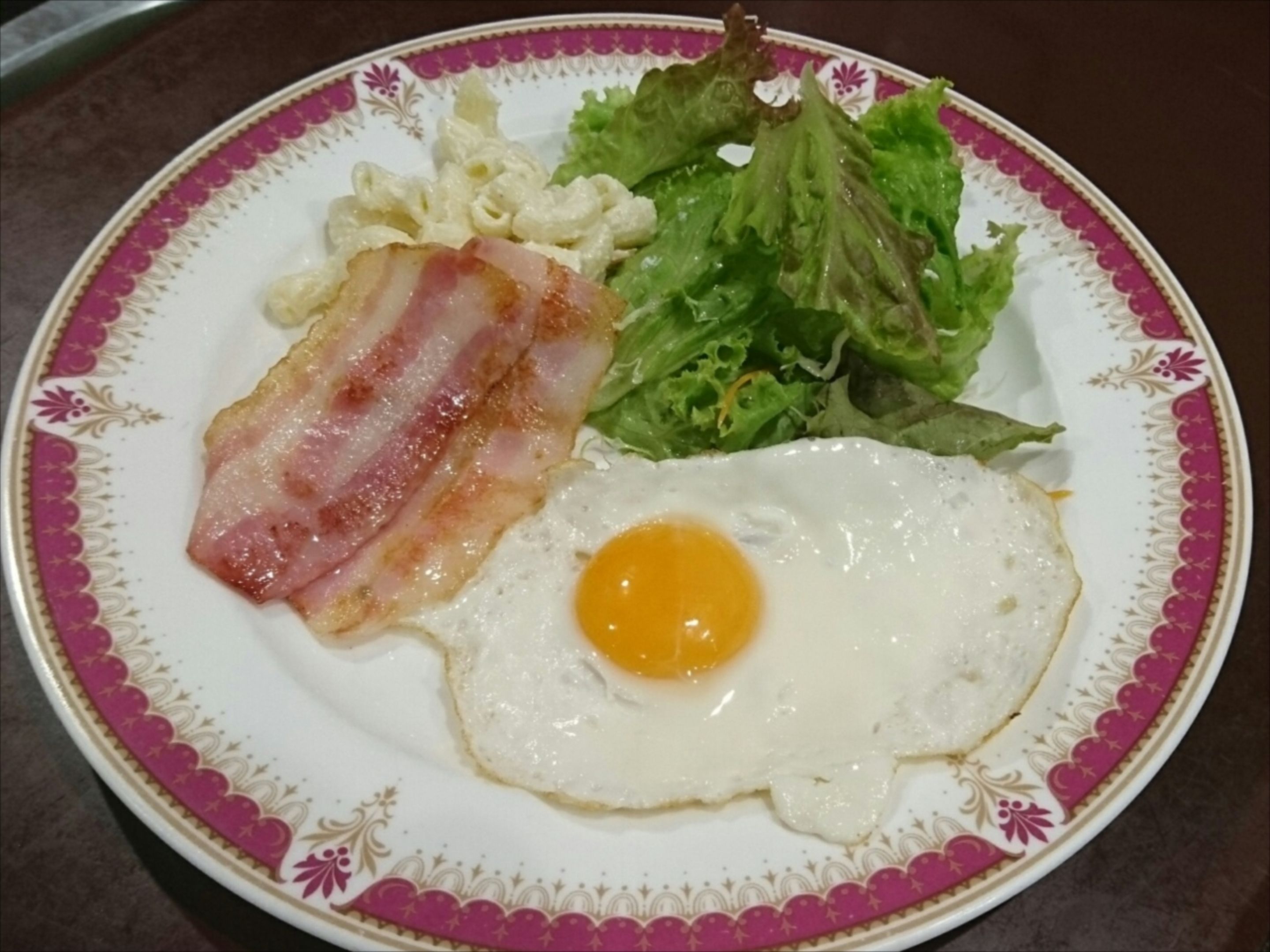 A plate with a fried egg, bacon, and a side salad.