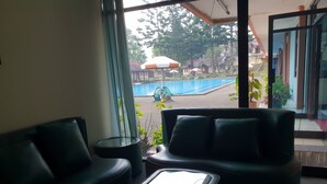 Un área de estar interior moderna con una mesa de centro de vidrio, ventanas amplias que ofrecen vista a una piscina y zona de estar exterior.