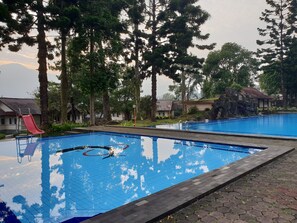 A swimming pool with a slide, surrounded by trees and a small building with a tiled roof. - Cisarua Indah Cottage (Cisarua)