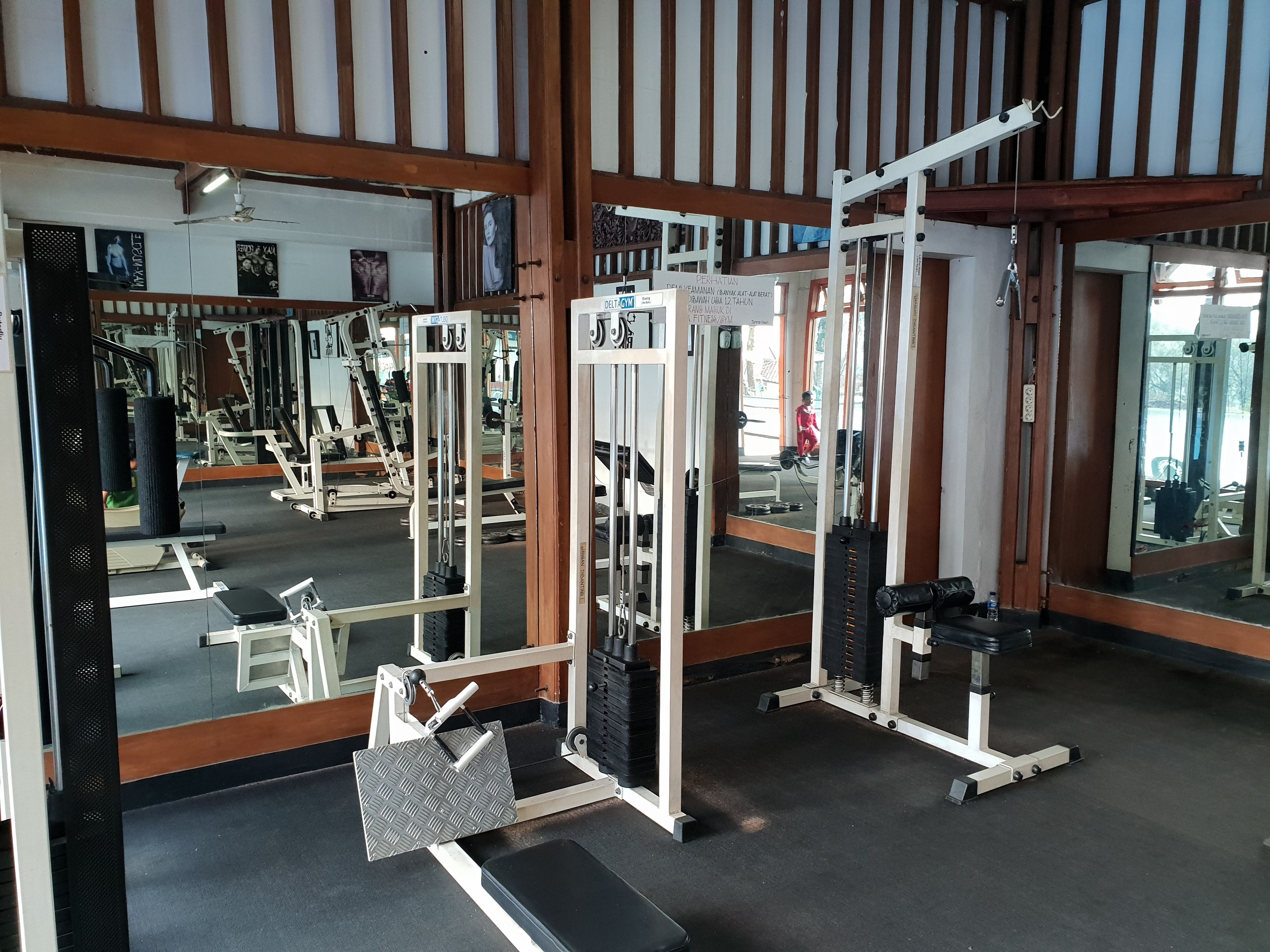 Un gimnasio con equipos de ejercicio variados, espejos y vigas de madera en el techo.