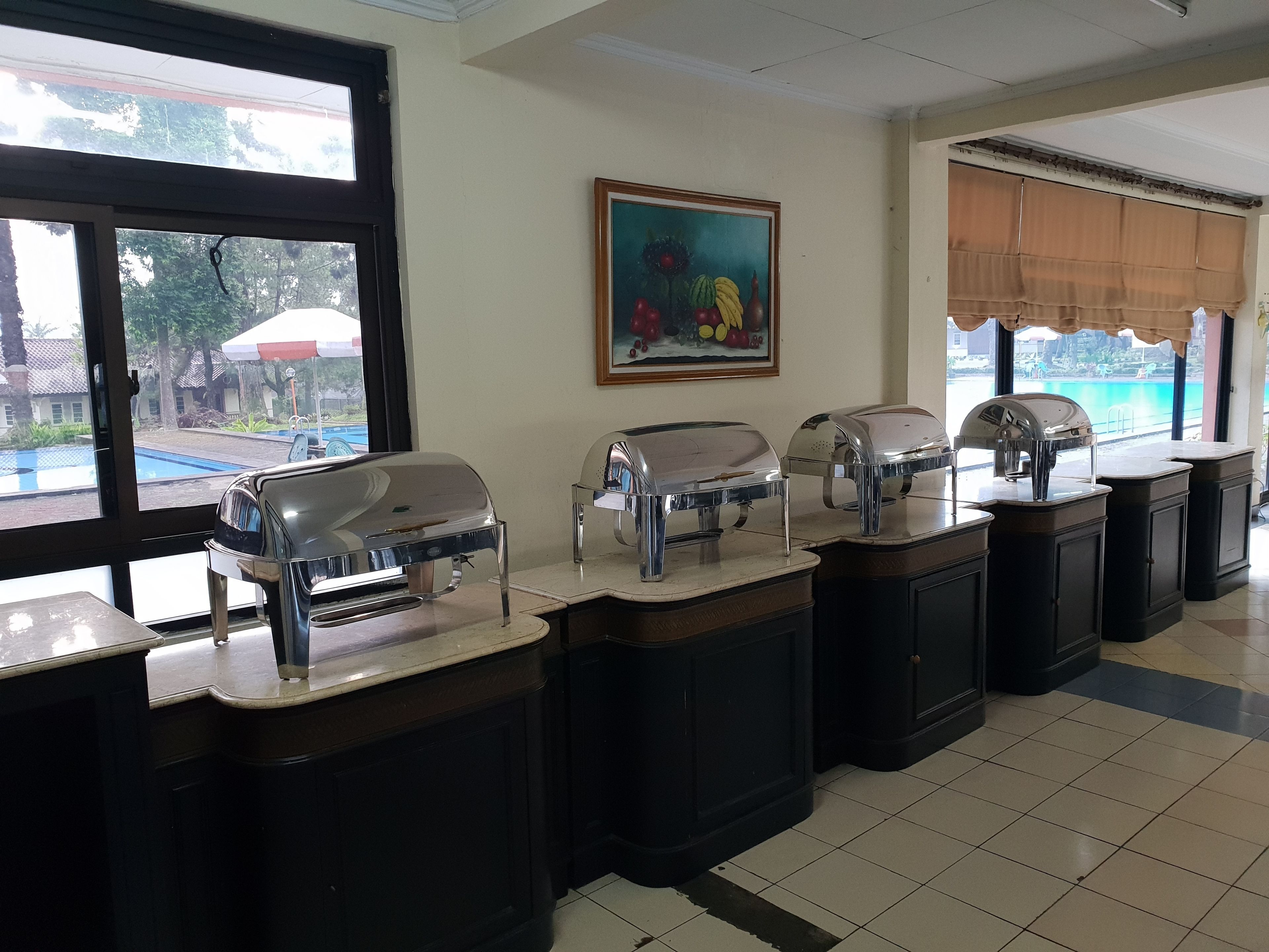 A buffet setup with multiple self-service stations, a painting on the wall, and a view of a swimming pool outside.