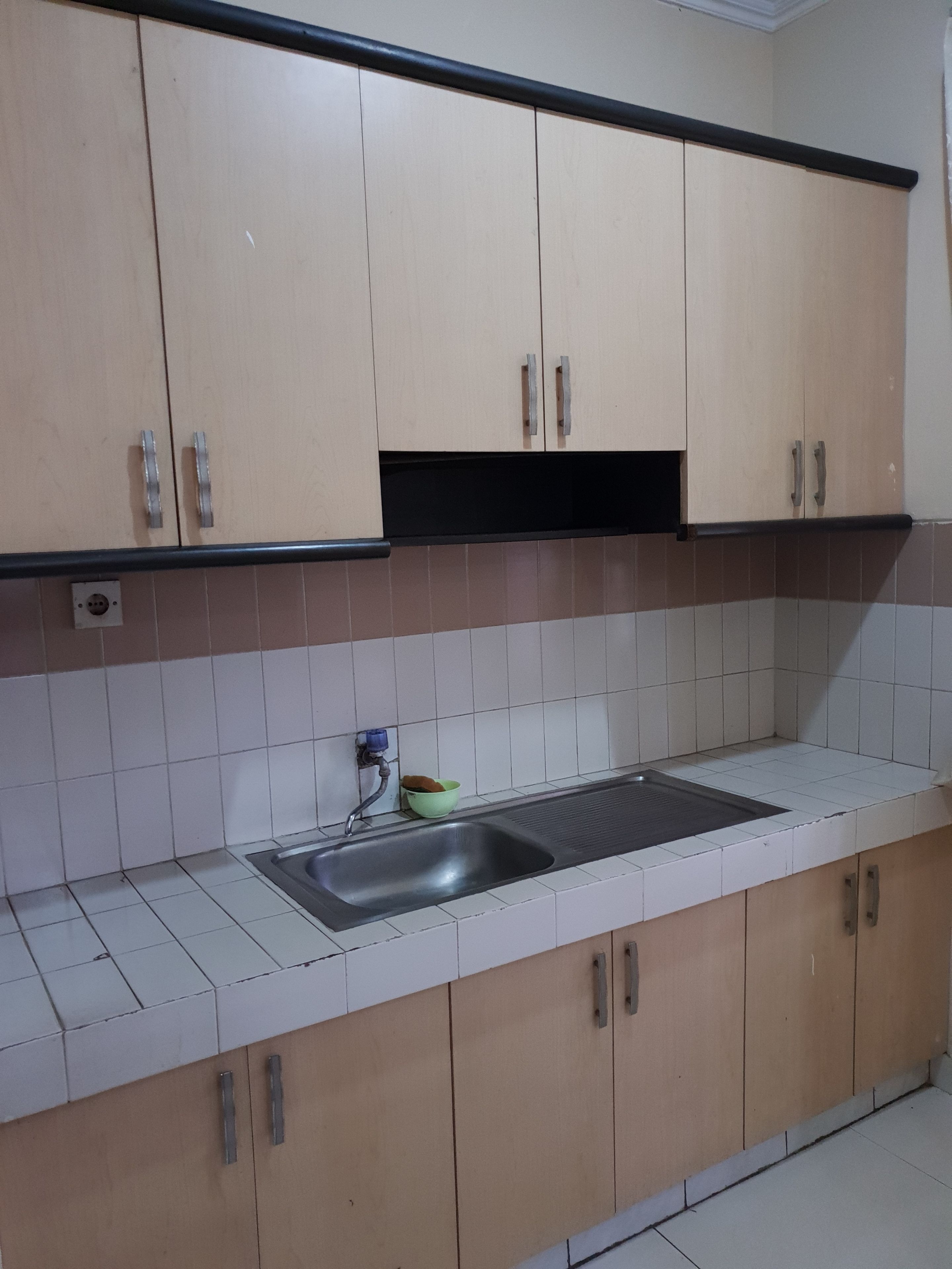 Una cocina con armarios color beige, un lavamanos de acero inoxidable y un protector de salpicadero con azulejos.