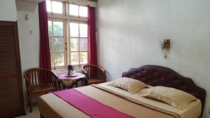 A hotel room with a bed, two chairs, a small table, and a window with curtains. - Hotel Royal Juanda (Jakarta)