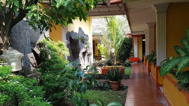 A covered walkway with potted plants, a rock wall, and a tiled floor. - Hotel Royal Juanda (Jakarta)