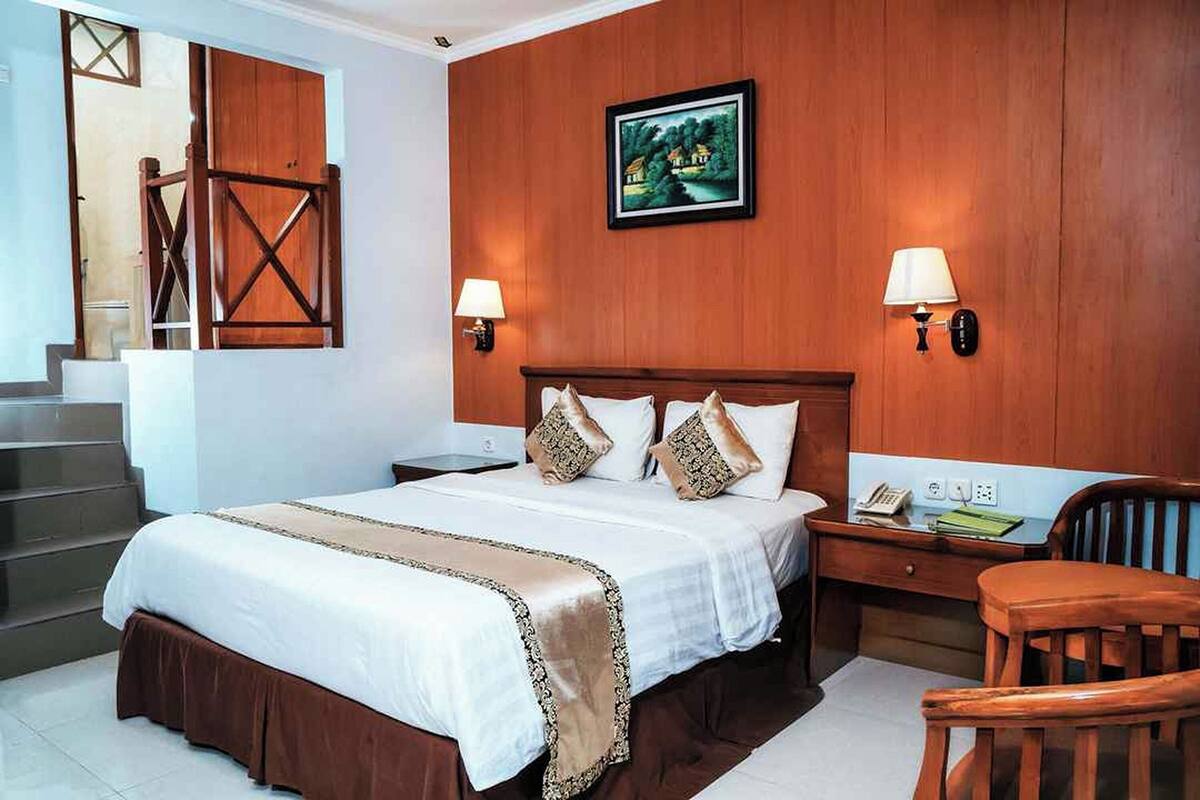 Een hotelkamer met een groot bed, twee nachtkastjes, een bureau en een stoel. Er is een trap die naar een hoger niveau leidt.