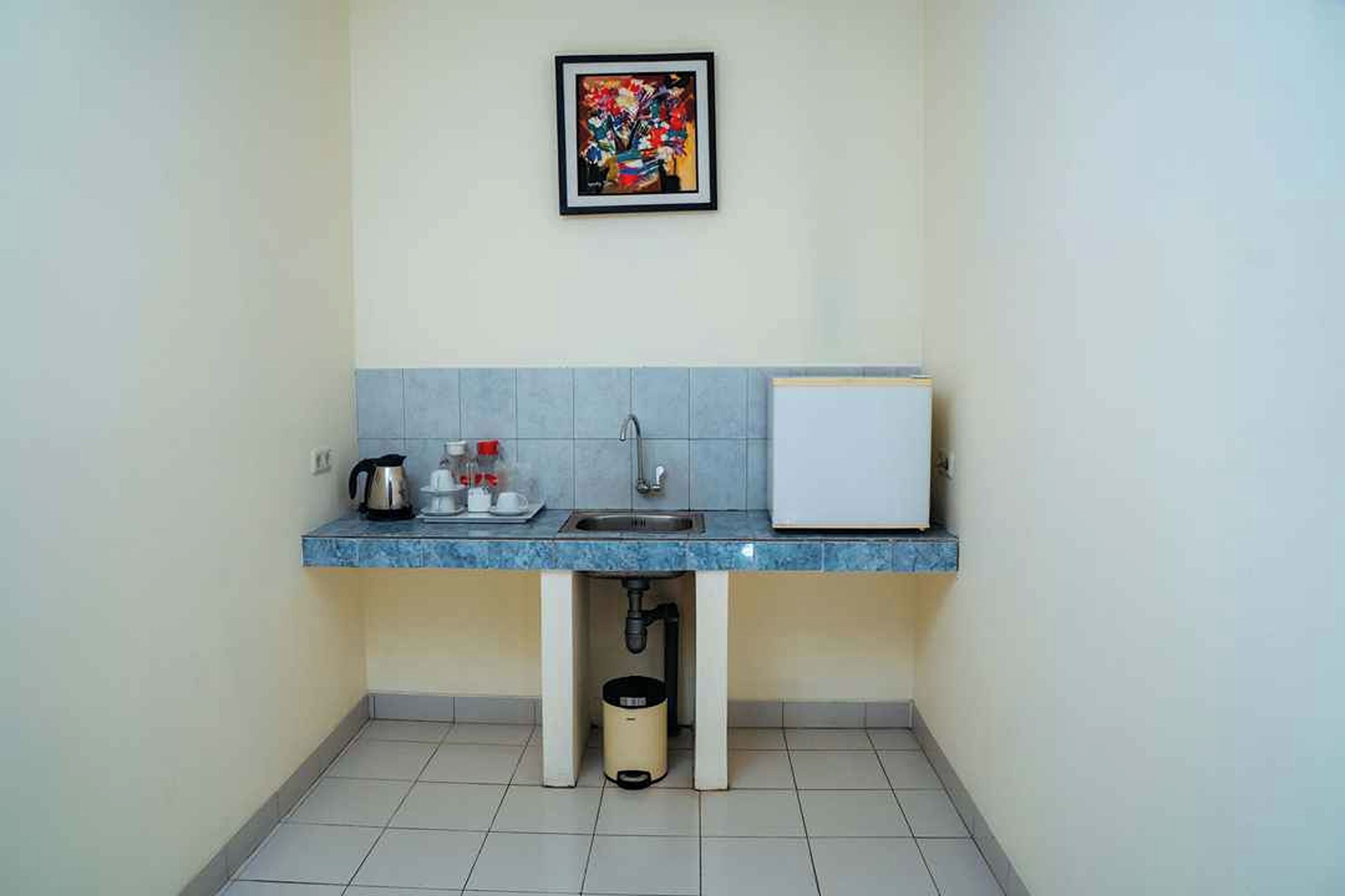 A small kitchenette with a sink, a kettle, and a refrigerator.