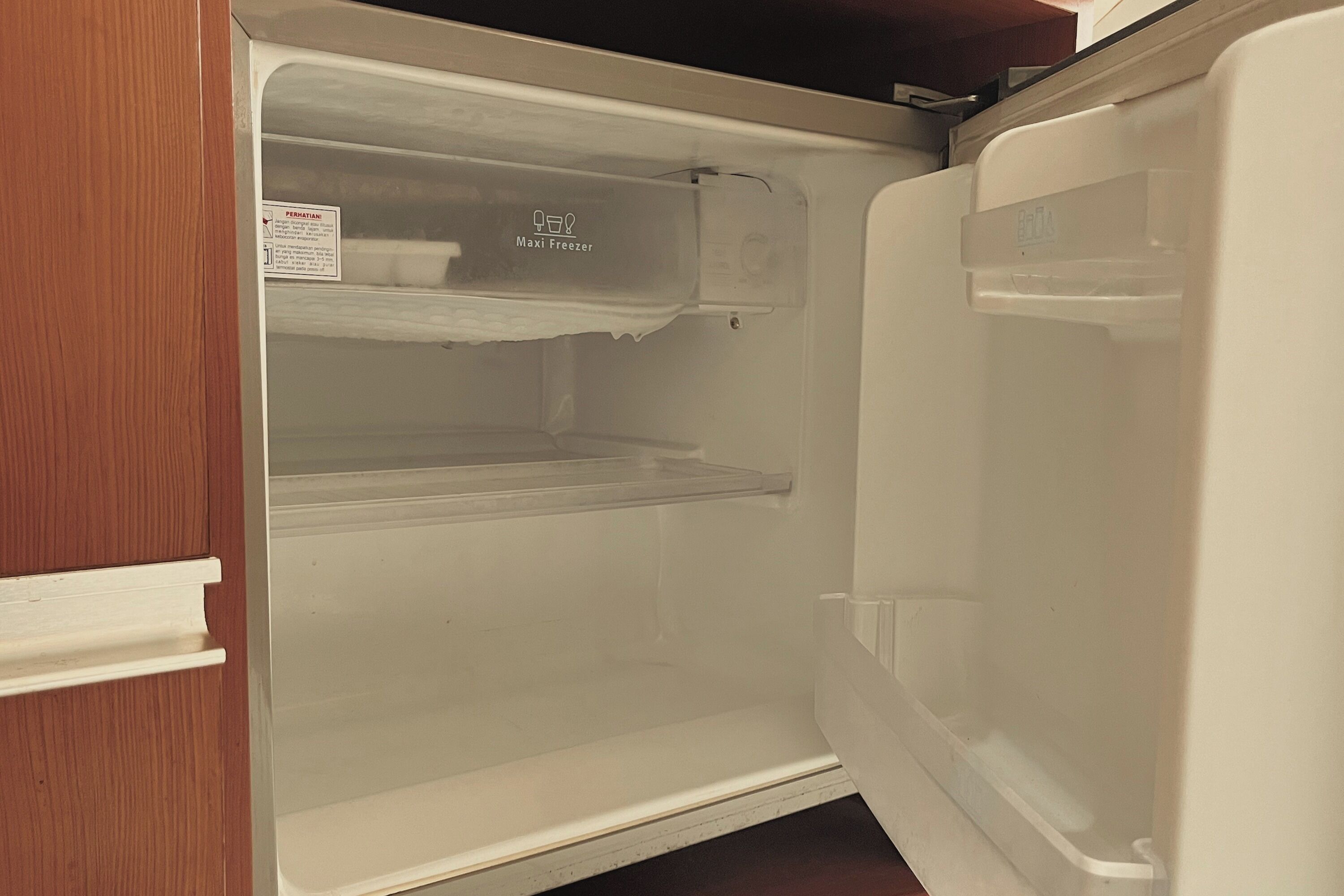 An open refrigerator with a 'Maxi Freezer' label, a warning label, and a clear shelf.