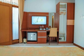 A hotel room with a wooden desk, a television mounted above it, a mini-fridge, a chair, and a wardrobe.
