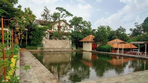 Une cour paisible, agrémentée d’une fontaine centrale, entourée de plantes en pot et d’un petit bâtiment doté d’un toit en tuiles.