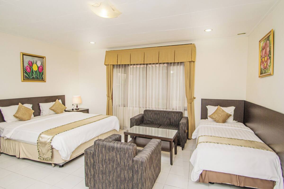 Een hotelkamer met twee bedden, een bank, een kleintje tafeltje en een raam met gordijnen.