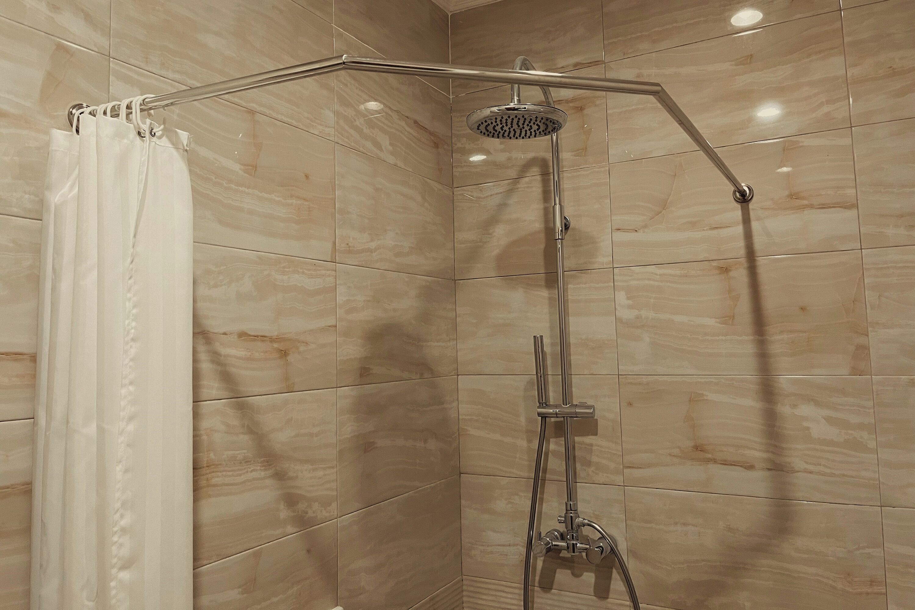 Une douche équipée d’un flexible incurvé et d’un pommeau de douche à main, le tout installé devant un mur carrelé.